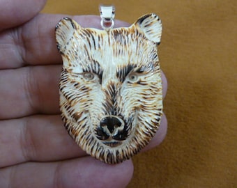 Puede incluir: Un colgante de cabeza de lobo tallado en hueso con una anilla de plata. El pelaje del lobo está detallado con marcas marrones y blancas. El colgante mide aproximadamente 5 cm de alto.