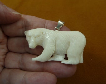 May include: A white carved polar bear pendant with a silver bail. The bear is standing on all fours and has a detailed face.