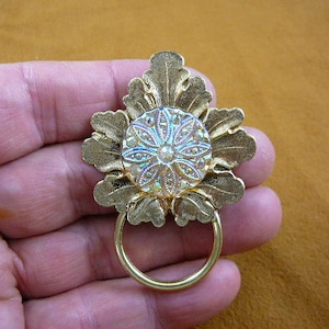 Peut inclure: Poignée de porte décorative en métal doré avec un motif floral et un centre iridescent. La poignée a une anse en forme d'anneau.