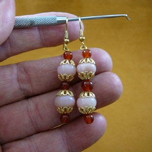 May include: Gold tone earrings with pink and brown beads. The beads are round and have a gold tone trim.