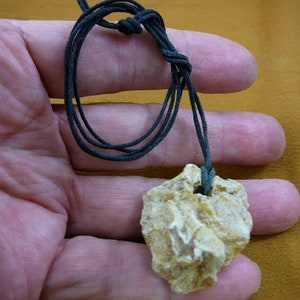 May include: A small, rough, light brown stone pendant on a black cord necklace.