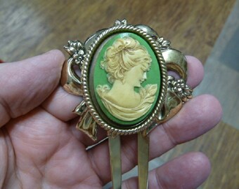 May include: Gold hair comb with a green cameo featuring a woman's profile.