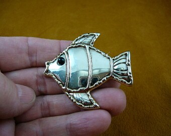 May include: Silver-toned fish brooch with a black eye. The fish has a detailed design with a textured surface.