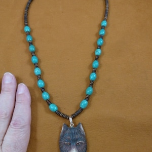 May include: A turquoise and brown beaded necklace with a carved wooden wolf pendant. The wolf's eyes are painted brown and the nose is white.