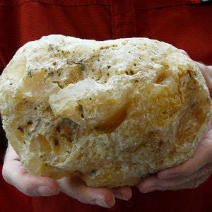 Peut inclure: Une grande géode d'agate de forme irrégulière, de couleur blanche et jaune. La géode a une surface rugueuse et texturée et est tenue dans deux mains.