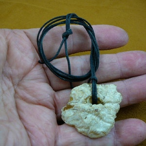 May include: A white, irregularly shaped stone pendant with a hole in the center, hanging from a black cord.