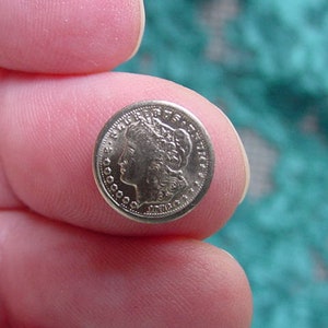 May include: A silver-colored coin with a woman's profile on the front. The coin is being held between two fingers.