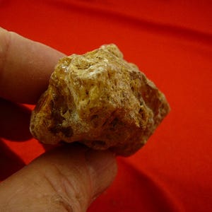 May include: A close-up of a rough, amber-colored rock with a textured surface. The rock is being held in a hand.