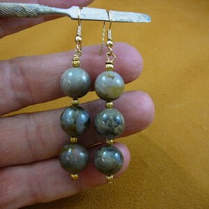 Peut inclure: Une paire de boucles d'oreilles en or avec trois perles rondes en agate grise et blanche sur chaque boucle d'oreille.