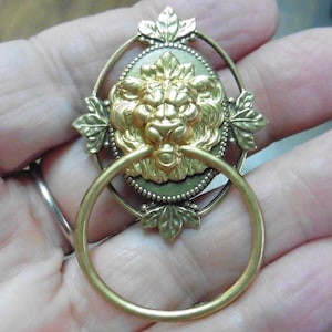 May include: An antique-style brass door knocker featuring a lion's head with a ring handle. The lion has a detailed mane and is set within an oval frame with leaf motifs. The knocker is likely made of brass.