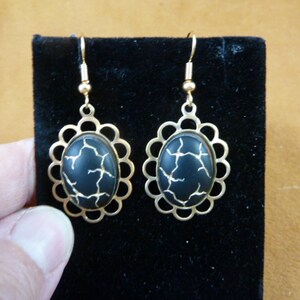 Puede incluir: Pendientes de tono dorado con piedras ovaladas negras con diseño de craquelado dorado.