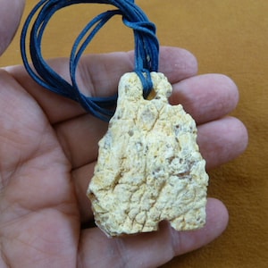 May include: A pale yellow, irregularly shaped pendant made of fossilized coral. The pendant is attached to a dark blue cord.