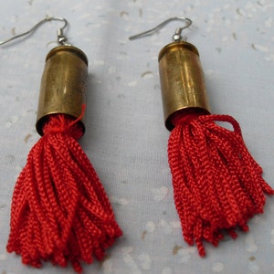 May include: A pair of earrings made from brass bullet casings with red tassel accents.