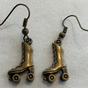 May include: A pair of bronze-colored roller skate earrings. Each earring features a detailed miniature roller skate charm with four wheels. The earrings have a simple hook design for easy wear, perfect for adding a touch of retro flair to any outfit.
