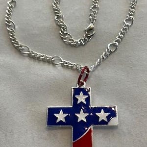 May include: A silver-toned chain necklace with a pendant in the shape of a cross. The cross features a patriotic design with blue, white, and red enamel, resembling the American flag. The pendant is approximately 2 inches in length.