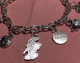 May include: A silver charm bracelet with various charms, including a soccer ball, a map of Scotland, a charm with the word "hope" on it, and a teapot charm.