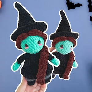 Può includere: Due bambole di strega all'uncinetto con pelle turchese, abiti neri e cappelli da strega neri. Hanno capelli e sciarpe marroni. Le bambole sono tenute in mano su uno sfondo blu con decorazioni di Halloween.
