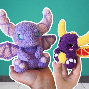 Puede incluir: Dos peluches de dragón hechos a mano con ganchillo. Uno es morado con detalles rosas y lavanda, el otro es más pequeño, morado con cuernos y detalles amarillos. Ambos tienen ojos grandes y están sobre un fondo turquesa.