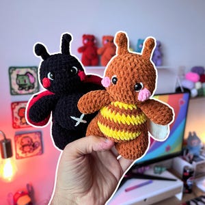May include: Two small, handmade crochet plush toys. One is a black ladybug with red wings and a white cross stitch on its chest. The other is a brown bee with yellow stripes on its abdomen, pink cheeks, and white wings. Both have black safety eyes.