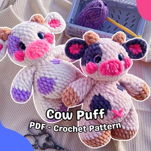 May include: Two handmade crochet cow plushies. The cows are white with purple and pink accents, and black eyes. The text "Cow Puff PDF - Crochet Pattern" is displayed below the plushies. A blue basket with purple yarn and a yellow crochet hook are in the background.
