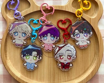 Può includere: Cinque portachiavi in acrilico raffiguranti personaggi in stile chibi con grandi occhi e capelli colorati, ciascuno fissato a un gancio a forma di cuore. I personaggi indossano pigiami e fasce per capelli in vari colori come viola, blu, rosa, rosso e giallo.