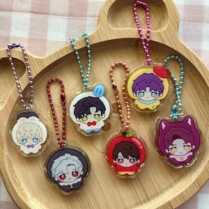 May include: Six acrylic charms featuring illustrated anime-style characters with colorful ball chains. The charms depict various figures, including one with a red apple hat, one with a blue popsicle, and one with purple cat ears, each attached to a metal chain.