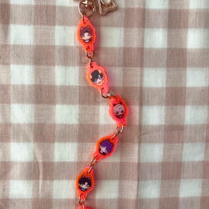 Pu&ograve; includere: Un portachiavi con una chiusura in metallo color oro rosa a forma di fiocco, collegata a una catena verticale di sei ciondoli in acrilico arancione neon. Ogni ciondolo raffigura un personaggio illustrato con orecchie da gatto, uniti da anellini.