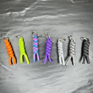 May include: Seven colorful paracord keychains with silver key rings. The keychains are made with different colored paracord and are tied in a knot pattern. The colors are orange, green, purple, blue, gray, gray, and black.