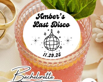 May include: White round sticker with black text and a disco ball graphic. The text reads "Amber's Last Disco 11.29.25". The sticker is on top of a pink cocktail in a glass. The text "Bachelorette Cocktail Toppers" is below the glass. A white circle with a martini glass graphic and the text "Drink Topper Depot" is in the lower right corner.