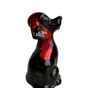 May include: A glossy glass figurine of a seated dog with a smooth, reflective surface. The sculpture features a striking color palette of deep black and vibrant red, with the red tones appearing as a translucent swirl within the dark glass body.