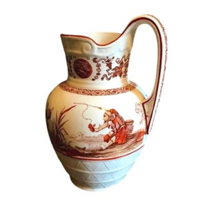 May include: Cream-colored ceramic pitcher with a detailed handle and a wide spout. The pitcher features a red and brown illustration of a person fishing, with decorative bands and floral patterns. The base has a textured design.