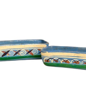 May include: Two rectangular blue ceramic planters featuring hand-painted designs. The left planter displays swirling patterns and dark shapes, while the right planter shows a series of arches over a green base. Both have cream-colored bands.