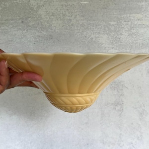May include: A pale yellow glass light shade featuring a wide, flared bowl shape with a subtle spiral fluted pattern. The base of the shade is decorated with a raised, rope-like textured band that encircles the bottom, providing a distinct visual detail.