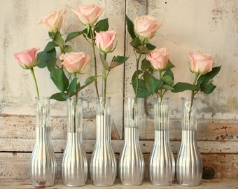 May include: Eight silver vases with a ribbed texture, each holding a single pink rose.