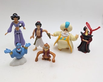 May include: A set of six plastic Disney Aladdin figures. The figures include Aladdin, Jasmine, Abu, Jafar, Genie, and the Sultan. The figures are all in various poses and are made of a bright, colorful plastic.