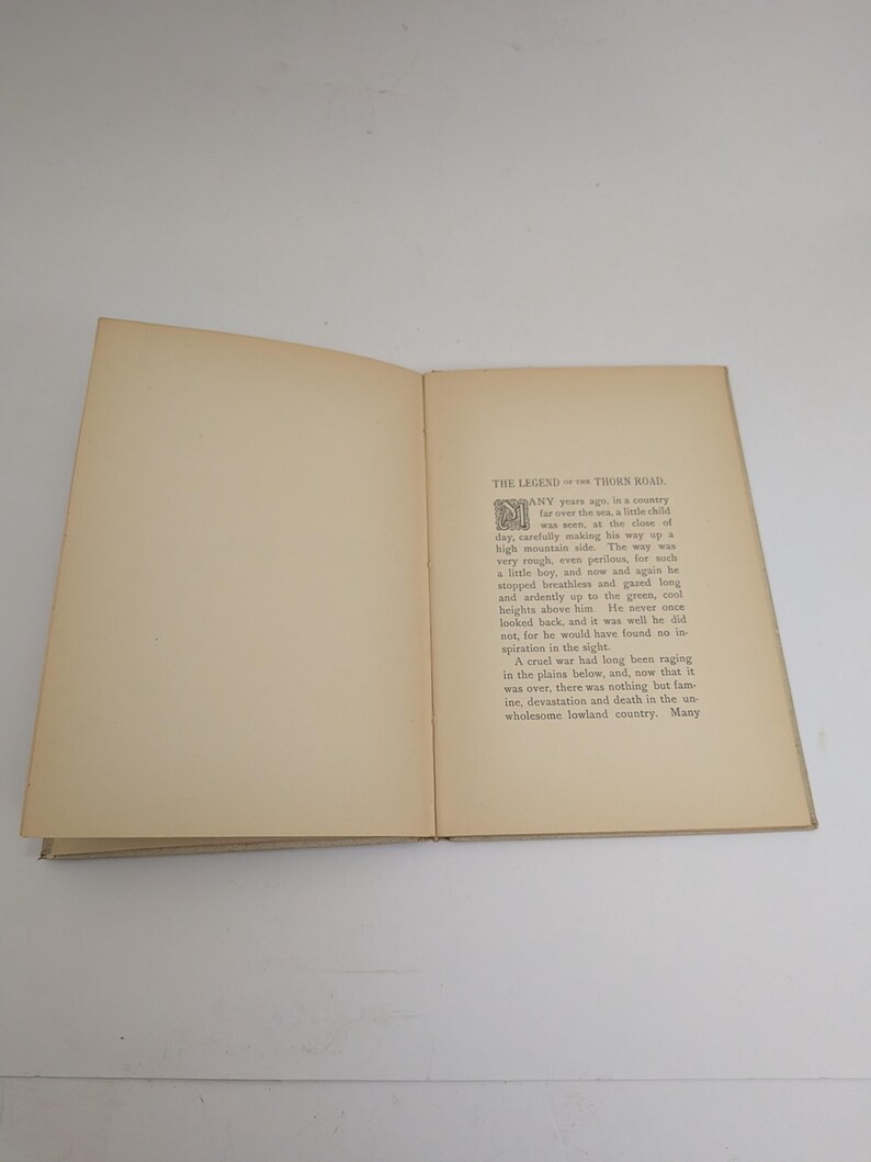 Pu&ograve; includere: Un libro aperto con pagine bianche sporche. Il testo sulla pagina di destra inizia con una grande iniziale decorativa. Il titolo "THE LEGEND of THORNS ROAD" &egrave; visibile in alto.