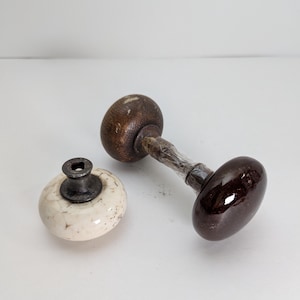 May include: Two antique door knobs. One is brown ceramic with a white glaze. The other is a wooden knob with a metal stem.