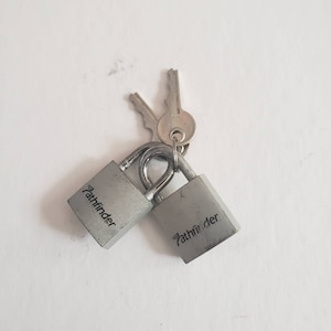 May include: Two silver padlocks with the word "Pathfinder" printed on them. The padlocks are attached to two keys.