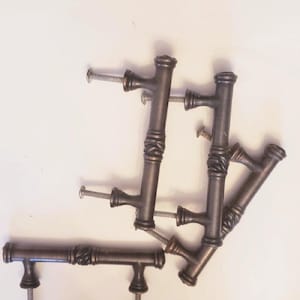 May include: Five antique bronze cabinet knobs with a decorative twisted design. The knobs have a T-shape with a screw on each end.