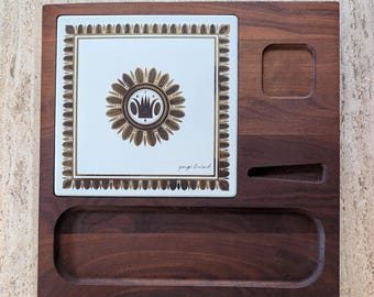 May include: A wooden serving tray with a white tile insert featuring a gold and brown floral design. The tray has a rectangular shape with a carved-out section and the signature "Jorge Briand".