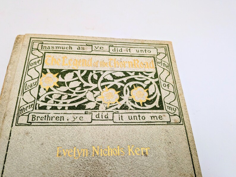 Pu&ograve; includere: Primo piano di un libro d'epoca intitolato "The Legend of the Thorn Road" di Evelyn Nichols Kerr. La copertina &egrave; bianco sporco con scritte dorate e decorazioni floreali verdi e dorate. Il titolo del libro &egrave; in oro.