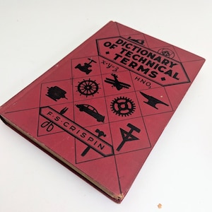 May include: A vintage red book titled "Dictionary of Technical Terms" by F.S. Crispin. The cover features black illustrations of various mechanical objects and mathematical symbols. The book is slightly worn, suggesting its age.