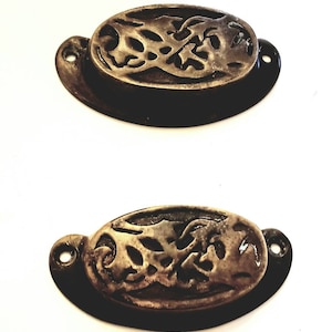 May include: Two oval-shaped, antique brass drawer pulls with an intricate, floral design.