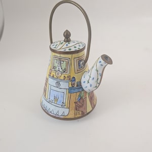 May include: A decorative teapot with a brass handle and spout. The teapot features a yellow body with a painted interior scene, a blue fireplace, and a patterned lid. The spout is white with blue floral accents. A charming collectible.