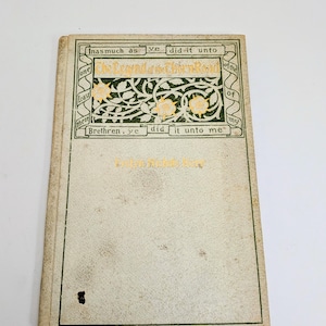Pu&ograve; includere: Libro d'epoca intitolato "The Legend of the Thorn Road" con scritte dorate e bordo decorativo verde e oro. La copertina &egrave; bianco sporco con macchie. Il titolo e una citazione religiosa sono visibili.
