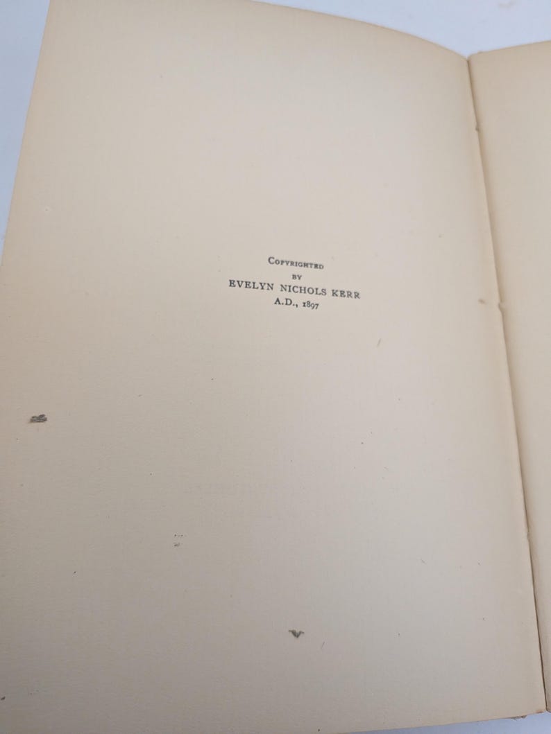 Pu&ograve; includere: Pagine di un libro aperto con il testo "Copyrighted by Evelyn Nichols Kerr A.D., 1897". Le pagine sono bianco sporco con alcune piccole macchie scure. Il testo &egrave; in un carattere serif.