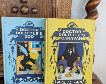 May include: Two vintage children's books by Hugh Lofting, "Doctor Dolittle's Zoo" and "Doctor Dolittle's Caravan". The books are yellow and blue with illustrations of animals and people.