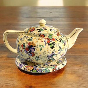 May include: A white ceramic mug with a black handle and the text "But First, Coffee" in a bold, black font. The mug is set against a blurred background, suggesting a cozy setting.