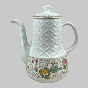 Puede incluir: Cafetera de cerámica blanca con un diseño de diamantes en el cuerpo y un diseño decorativo de pájaros y flores alrededor de la base. La tapa y el borde presentan un diseño de remolino marrón y dorado. La cafetera tiene un pico y un asa curvados.