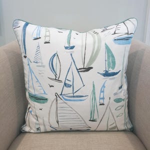 May include: A white throw pillow with a blue and green sailboat pattern. The pillow has a light green border.